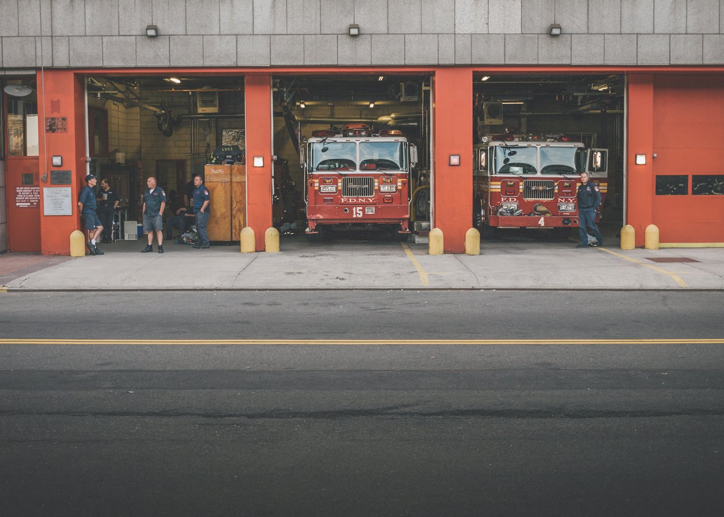 Firefighters standing outside a station with fire trucks inside.